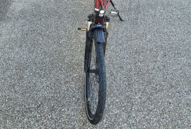Ein rotes Fahrrad auf der Straße mit einem offensichtlichen Schaden am Vorderreifen.