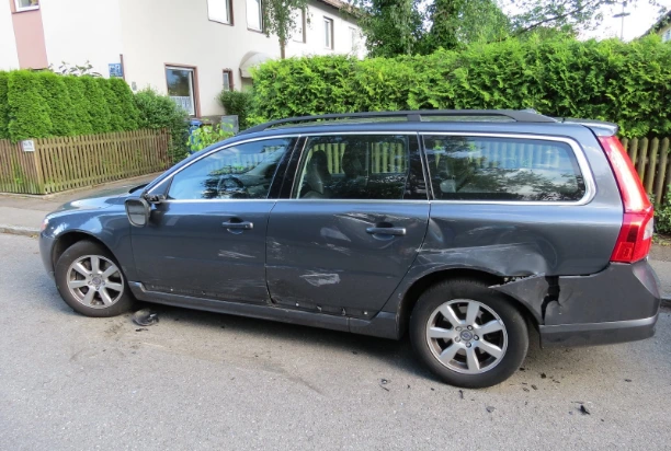 Ein graues Auto von der Seite bei dem die komplette Seite aufgrund eines Unfalls beschädigt ist.
