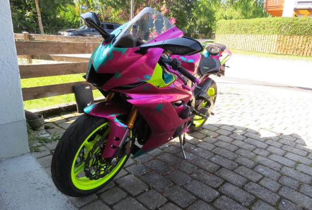 Ein pinkes, getuntes Motorrad mit türkisenen Farbspritzern und neongelben Reifen, das für ein Motorradgutachten aufgestellt wurde.